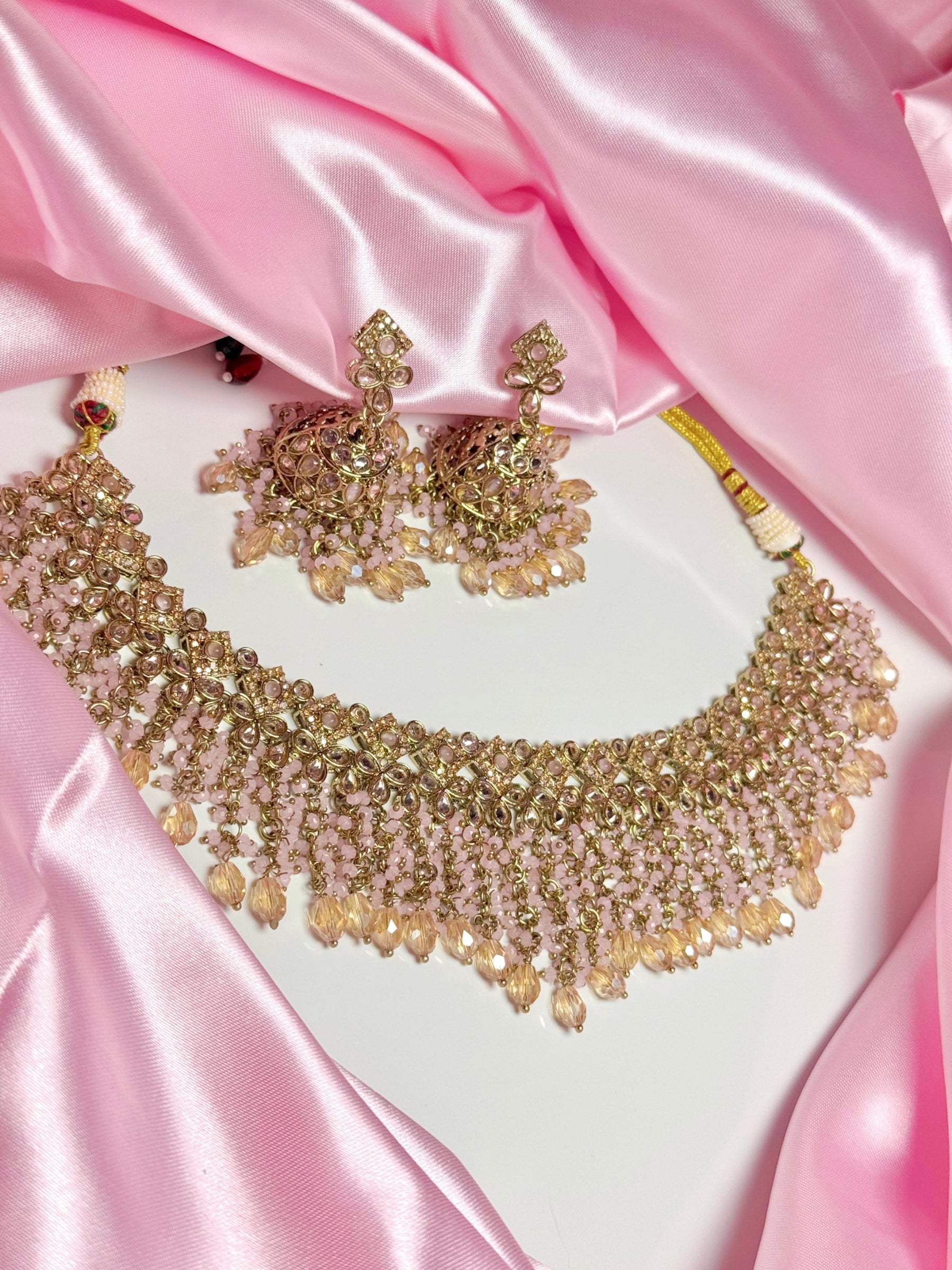 Gold necklace and earrings on a pink satin background